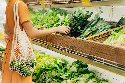 Woman Holding Mesh Shopping Bag In Produce Section Of Grocery Store