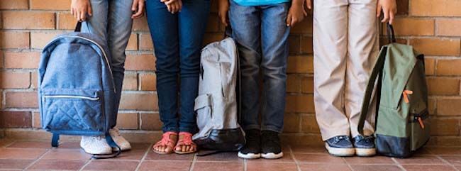  elementaryBack to school students standing outside class with backpacks.