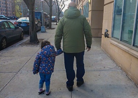 Child and adult walking on sidewalk, holding hands
