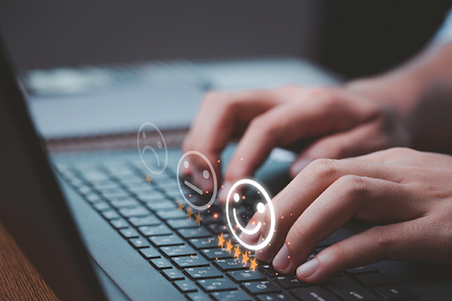 Person using a laptop selecting a smiley face icon with five yellow stars while taking an at-home survey.
