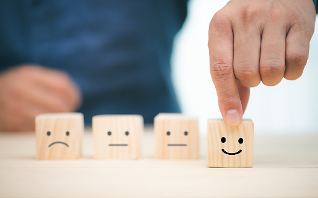 A person chooses a smiley face on wood block cube indicating customer satisfaction.