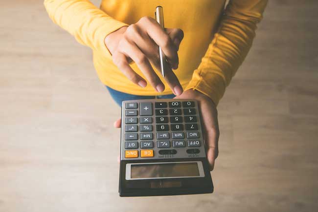 A person in a yellow sweater holding a pen and calculator. 