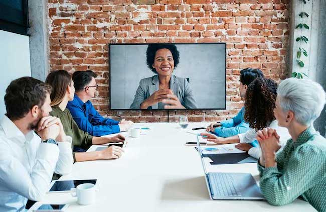 A group of employees facing a monitor showing a customer offering her thoughts.