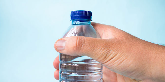 A hand holding a plastic water bottle with a blue cap.