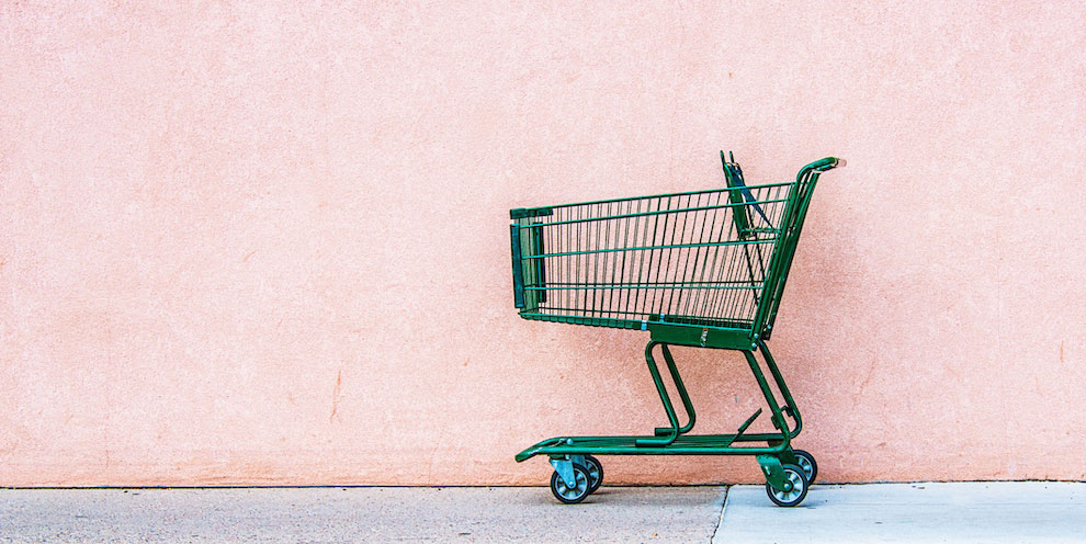 A green shopping cart in front of a pink wall.