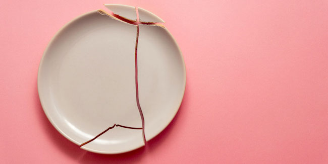 A shattered white plate on a pink background.
