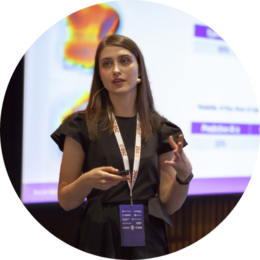 An action shot of Milica Kovac speaking at an event with a slide behind her.